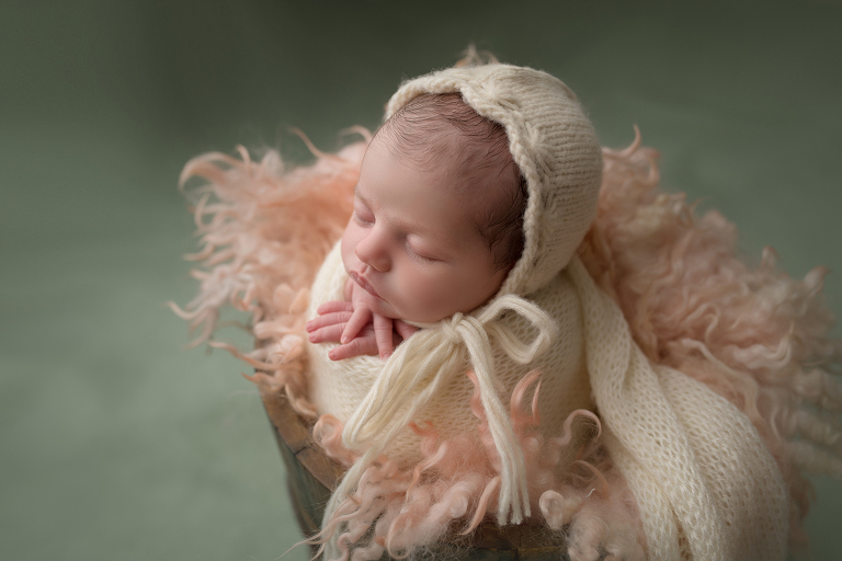 Newborn baby posed in curly fur inside bucket