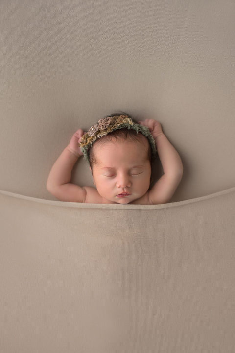 Baby girl sleeping under blanket with arms stretched